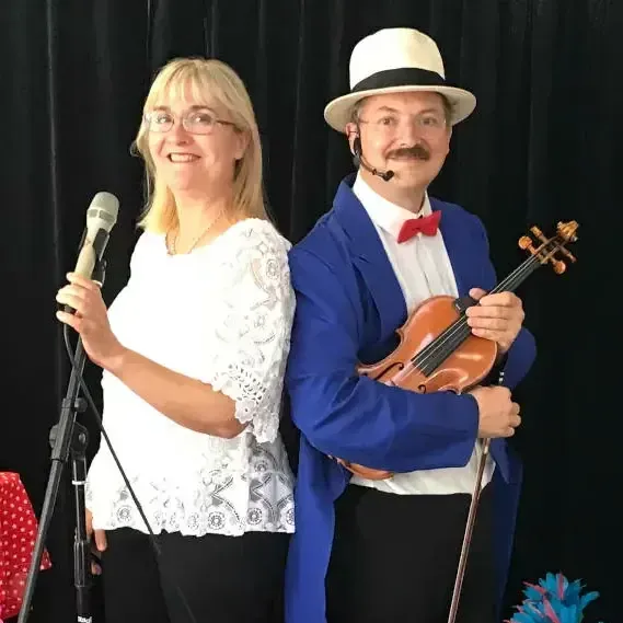 Nathalie au micro et Sylvio au violon, dos à dos, devant un rideau noir