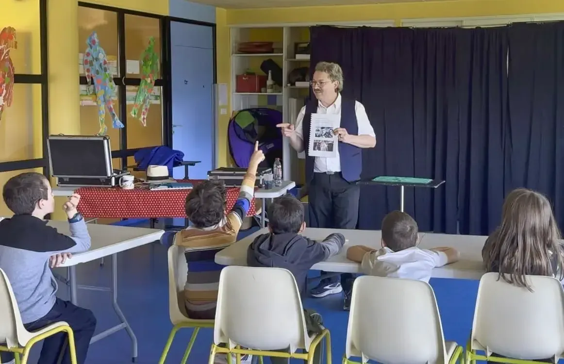 Sylvio présente un document à des élèves assis dans une salle d'activités, pendant l'atelier de magie