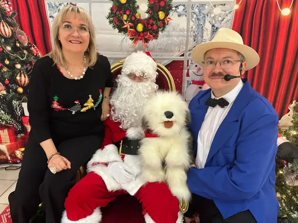 Nathalie, le Père Noël et Sylvio en veste bleue posent devant un sapin, avec la marionnette d'un chien blanc