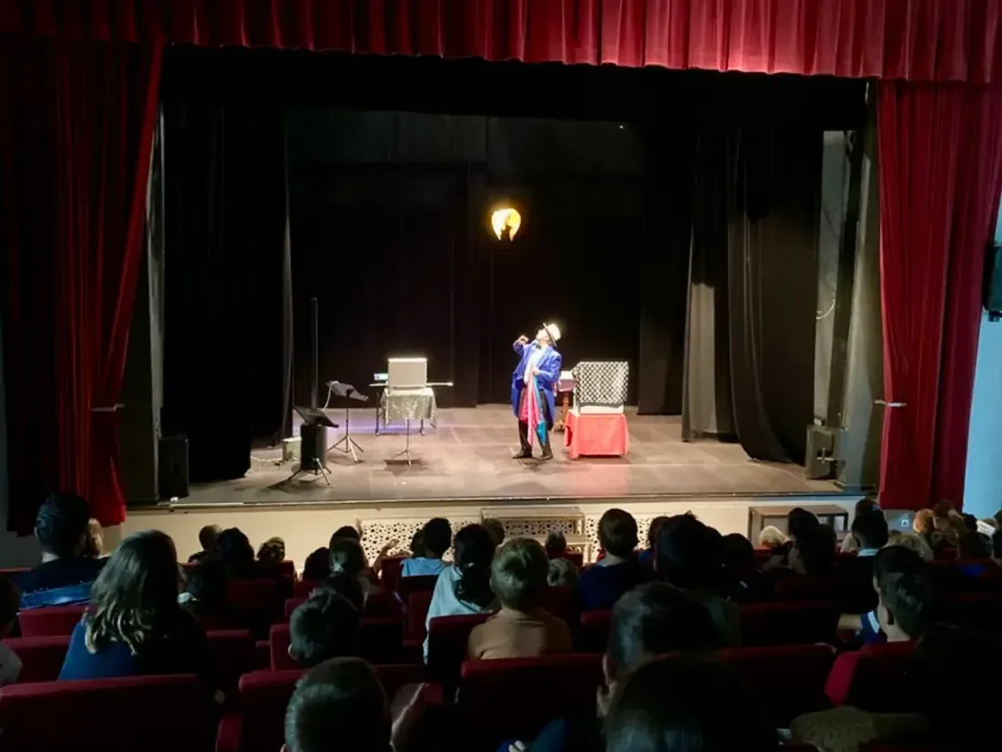 Sylvio seul sur la scène d'un théâtre à rideau rouge, face à une salle pleine