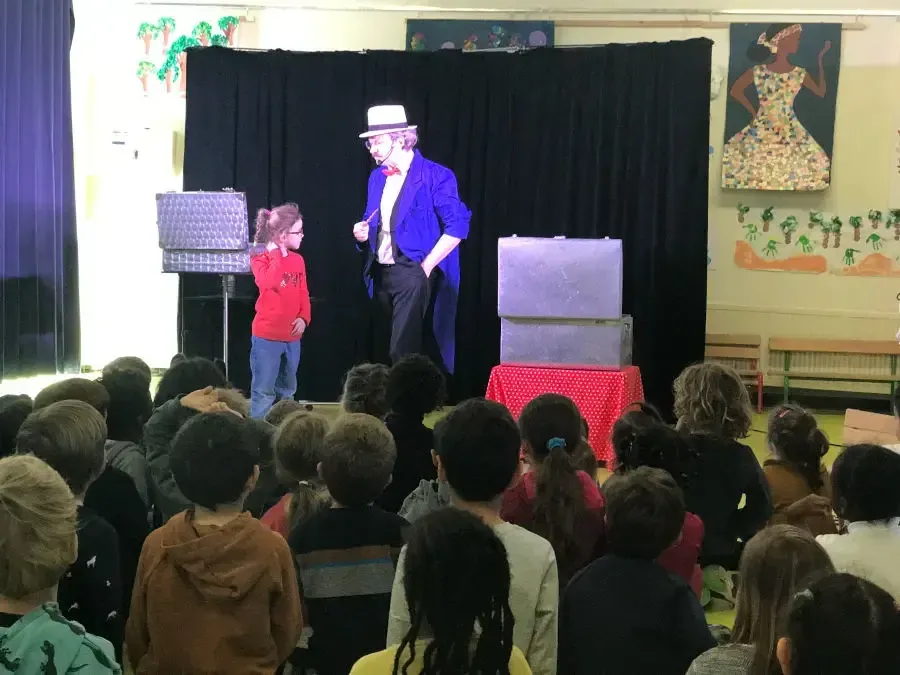 Sylvio le magicien sur scène en queue de pie bleue devant un public d'enfants installés dans une salle