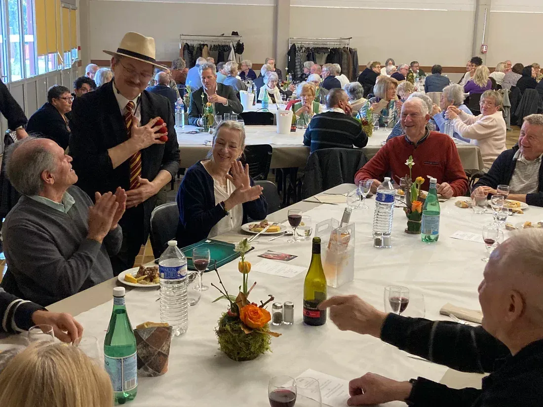 Sylvio, chapeau panama, fait applaudir une tablée d’aînés lors d’un repas dans une salle communale