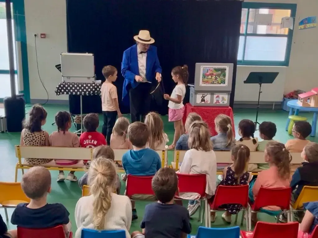 Une enfant, de dos, aide Sylvio sur scène devant ses camarades assis