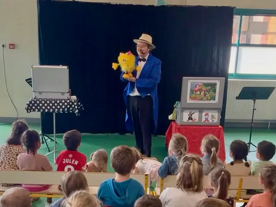 Sylvio présente Youmi, sa marionnette jaune, devant des enfants assis sur des bancs
